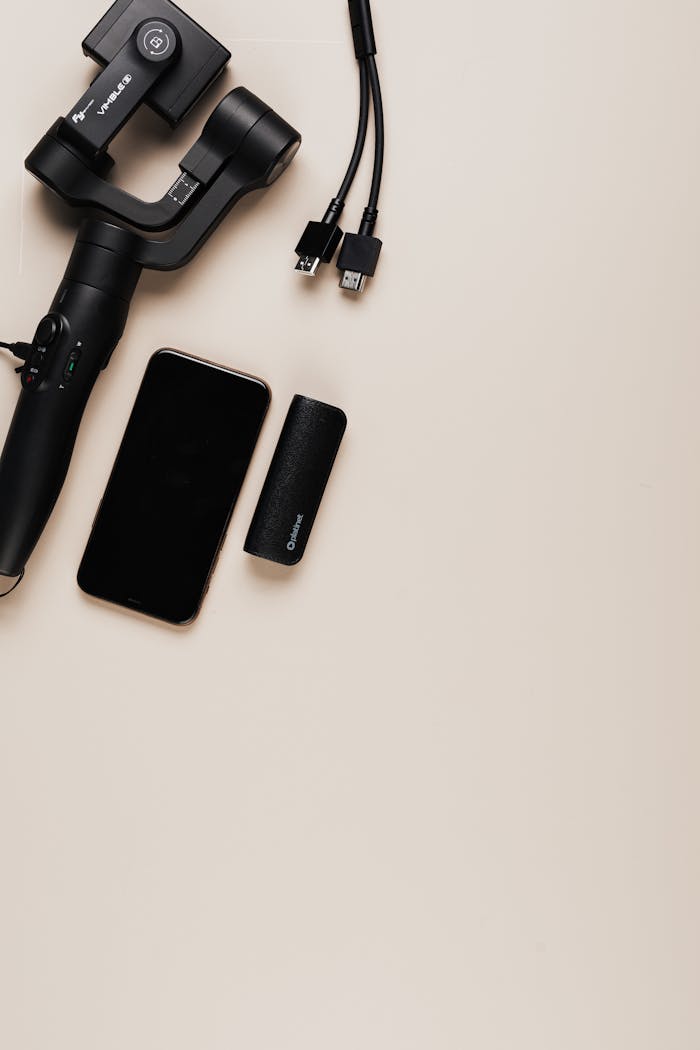 Top view of a smartphone, gimbal, power bank, and cables on a beige background.