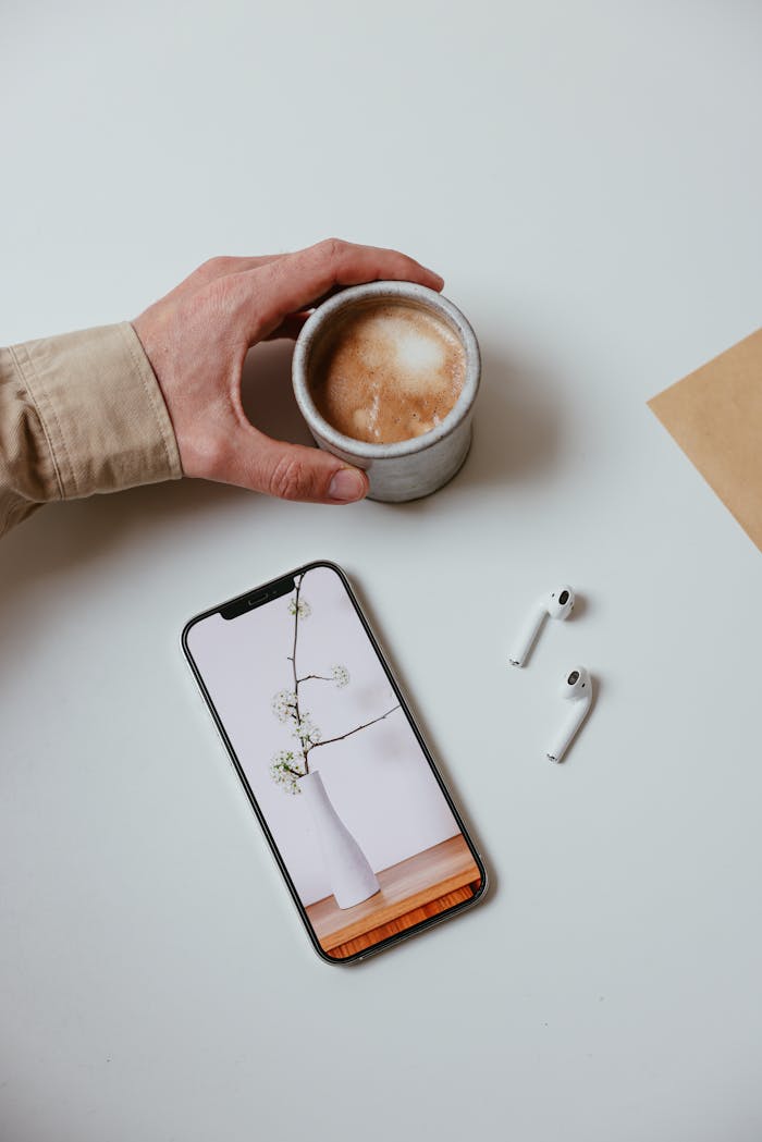 Modern desk setup featuring a smartphone, coffee cup, and earpods for a trendy work environment.